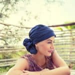 Woman wearing a blue turban with a patterned top outdoors.