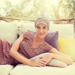 Woman wearing a beige turban and colorful dress on outdoor sofa.