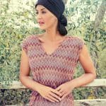 Elegant woman wearing a black turban and patterned dress outdoors.