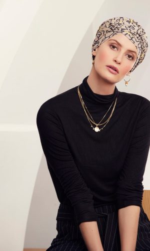 Woman wearing a patterned turban and black top, sitting on a wooden chair.