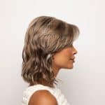 Side view of a woman wearing a wavy, ash blonde wig from the Noriko Collection.