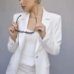 Elegant blonde wig styled on a woman in a white suit, holding glasses.