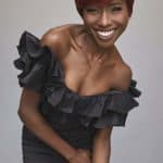 Elegant woman with short red wig and black ruffled dress smiling.