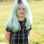 Young girl with mint green and silver wig outdoors, smiling happily.