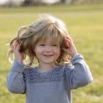 Adorable girl wearing a wavy blonde wig outdoors in a park setting.