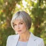 Elegant short gray wig on a woman outdoors with greenery.