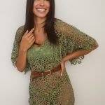 Woman with long dark hair wearing a green lace dress smiling at camera.