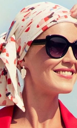 Woman wearing a patterned headscarf and large sunglasses, smiling outdoors.