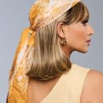 Side view of woman wearing a blonde wig with a yellow patterned headscarf.