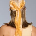 Back view of woman wearing a yellow headscarf and wig for a natural look.