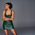 Model with coily, curly ponytail wearing a green dress against gray background.