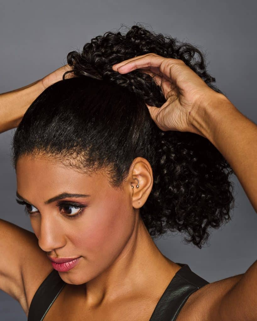Woman wearing a coily, cinched ponytail wig with natural curls.