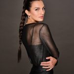 Woman with long braided wig in a black sheer top and dark background.