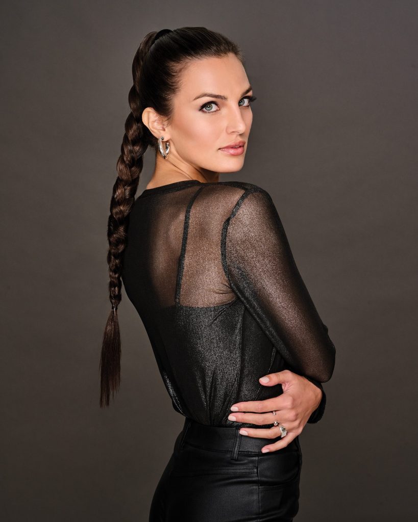 Woman with long braided wig in a black sheer top and dark background.