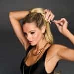 Woman styling a blonde Hollywood Waves Cinch Pony wig with a curling iron.