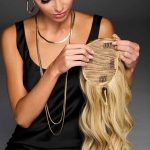 Woman holding a blonde wig with Hollywood waves and a cinch ponytail style.