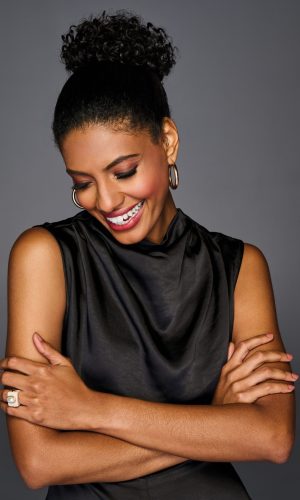 Beautiful woman with coily wrap wig, smiling and looking down.