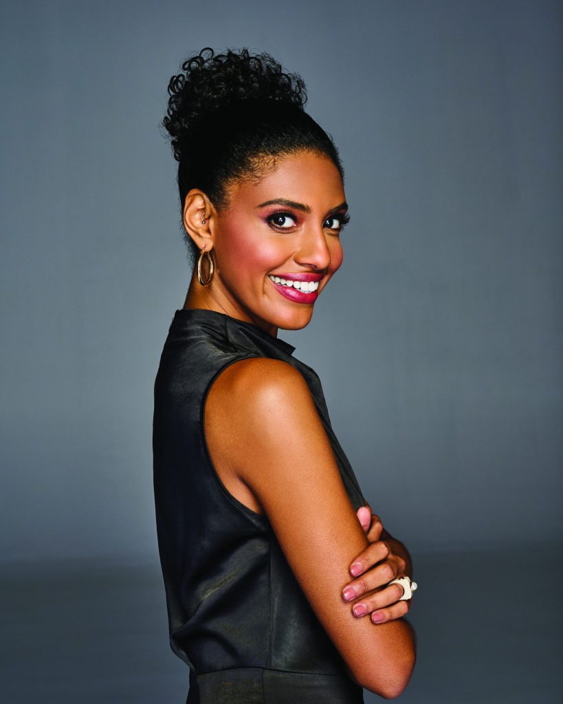 Woman with coily curly wig styled in a high bun, smiling confidently.