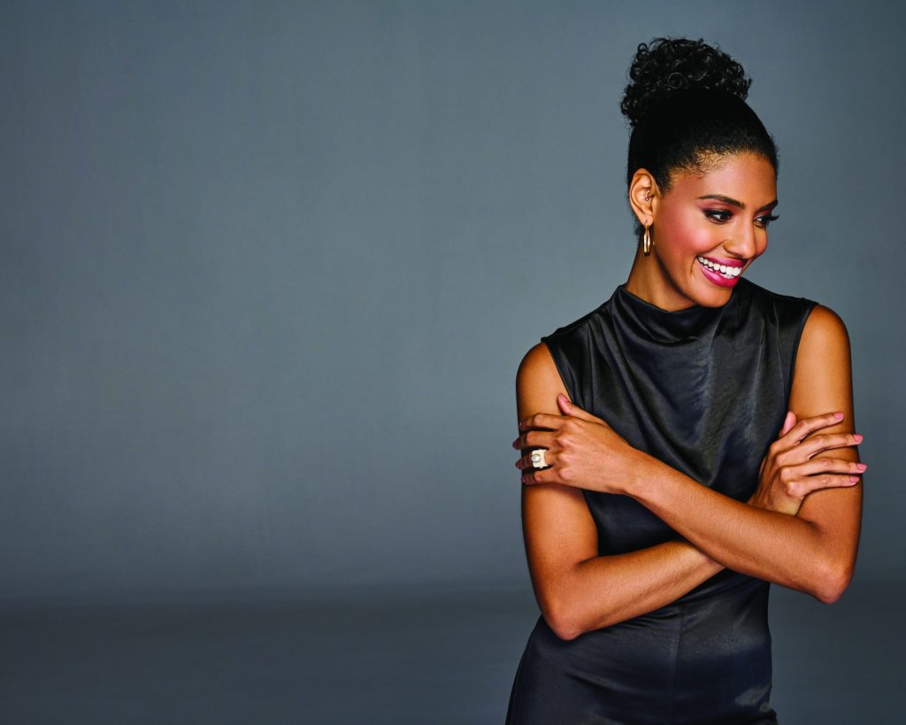 Woman with coily wrap hairstyle, smiling, wearing black sleeveless top.