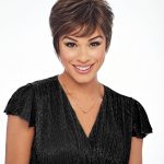 Woman with short brown pixie wig, smiling, wearing black dress.