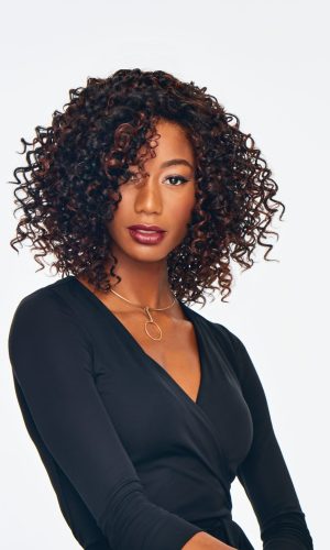 Woman with curly wig and black outfit, looking confident.