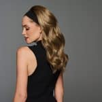 Woman with long, soft curled wig and headband, side profile view.