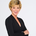 Woman with short, layered blonde wig and black top smiling.