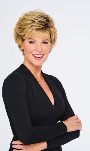 Woman with short, layered blonde wig and black top smiling.