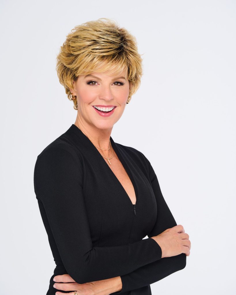 Woman with short, layered blonde wig and black top smiling.