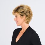 Side view of a woman with a short, curly blonde wig and black outfit.