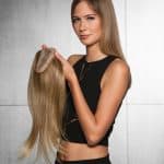 Young woman holding a blonde wig on a wig stand, showcasing hair extension options.