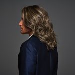 Side view of a man with wavy brown wig and long hair.