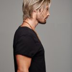 Side view of a man with blonde wavy wig and black t-shirt.