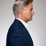 Side profile of a man with silver wig in a blue suit.