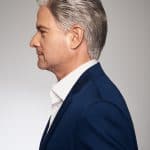 Side profile of a man with silver hair wearing a blue suit and white shirt.