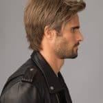 Side profile of a man with styled blonde wig and leather jacket.