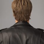 Back view of a man with short, layered brown wig in a leather jacket.