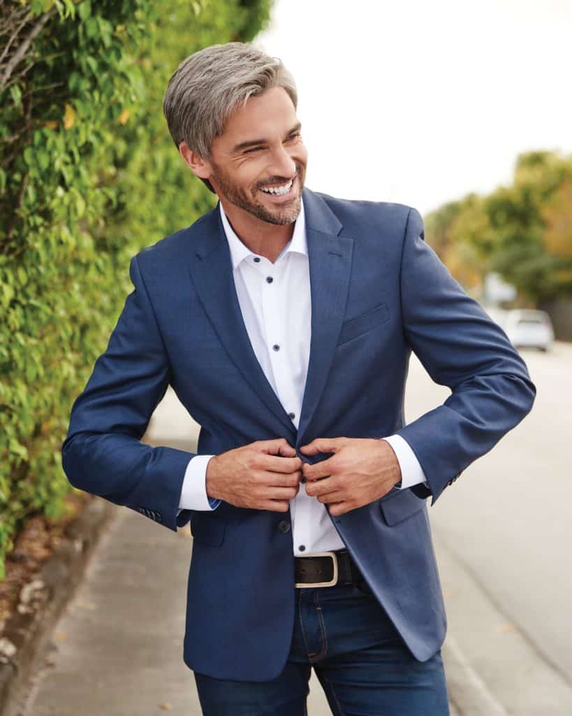 Smiling mature man in blue suit adjusting his jacket outdoors.