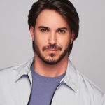 Man with styled dark hair and beard wearing a light jacket and blue shirt.