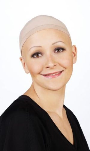 Woman wearing a beige wig cap and black top, smiling at the camera.