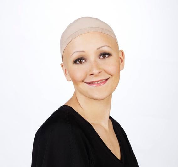 Woman wearing a beige wig cap and black top, smiling at the camera.