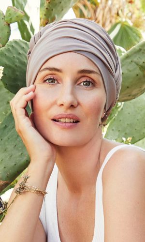 Woman wearing a stylish beige turban in front of cactus plants.