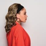 Side view of woman wearing wavy headband wig with black headband and hoop earrings.
