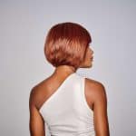 Side view of a woman with a sleek, short, copper-colored wig.