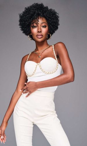 Model wearing a curly black wig with stylish outfit and accessories.