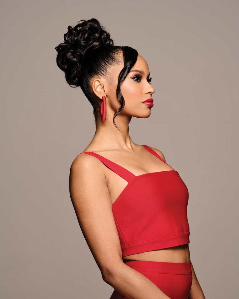 Woman with an elegant curly updo wig, red top, and matching earrings.