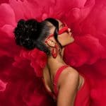 Side profile of a woman with a sleek black updo wig and red accessories.