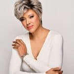 Elegant woman with short silver wig and white top, looking confident.