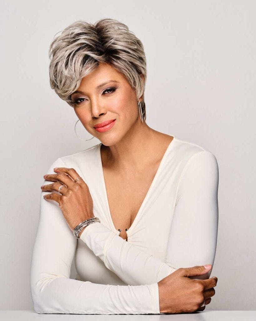 Elegant woman with short silver wig and white top, looking confident.