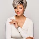 Elegant short gray wig styled on a mature woman with makeup and hoop earrings.